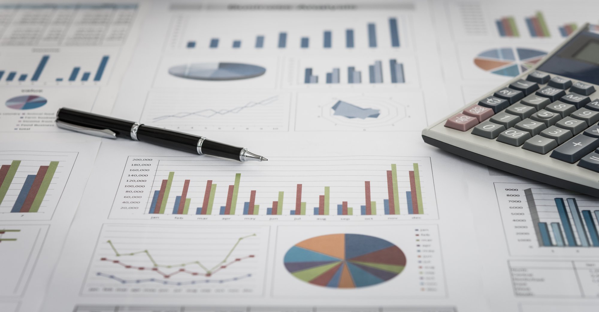 A collection of documents with charts on them with a calculator and pen laying on top.