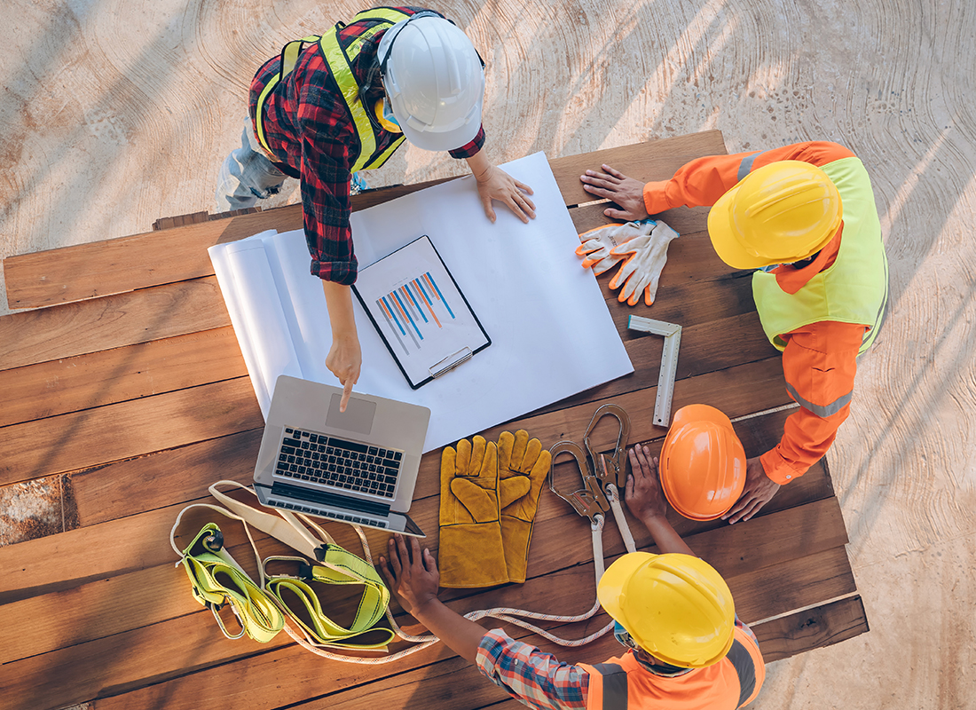 Three construction workers review blueprints and a laptop.